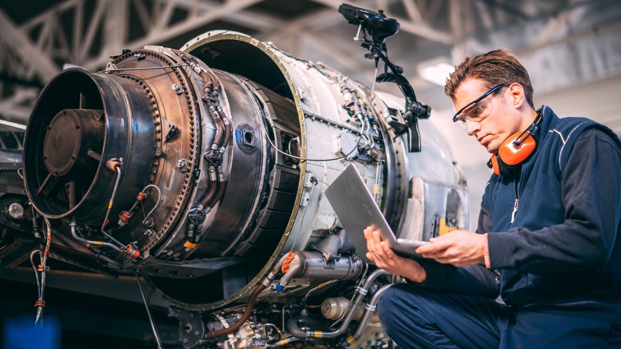 Photo of male mechanic in front of aircraft propellor looking at laptop