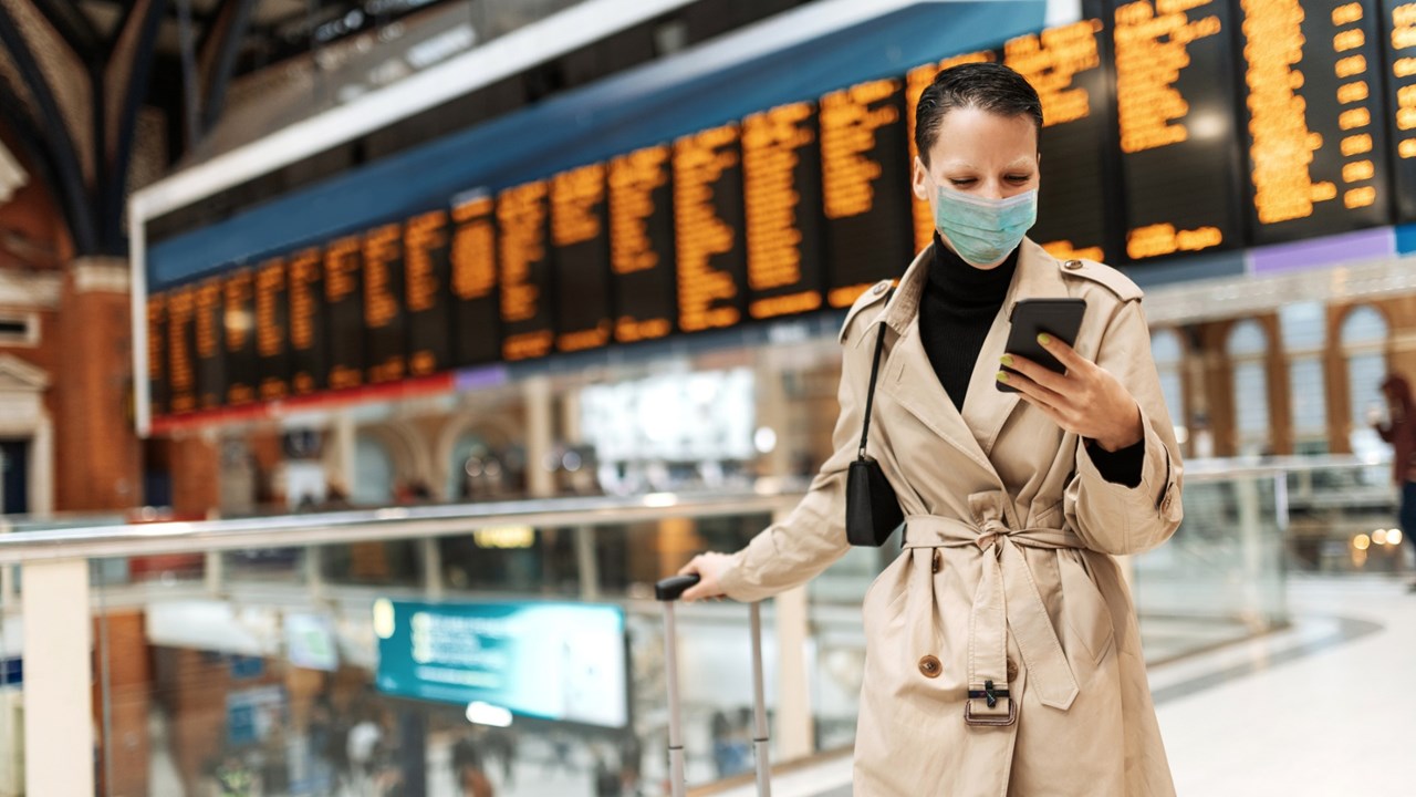 Photo of face-masked woman using phone at airport terminal